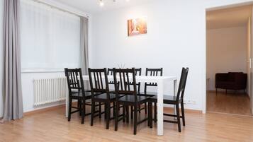 Ein Essbereich mit einem weißen Tisch und dunklen Holzstühlen, einem Heizkörper, einem Fenster mit Vorhängen und einem Gemälde an der Wand.