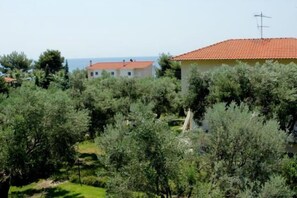 A residential area with houses surrounded by dense greenery and a clear view of the sea in the background.