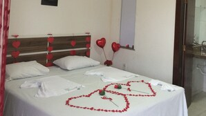 A hotel room with a bed, a bedside table, a mirror, and an air conditioning unit.
