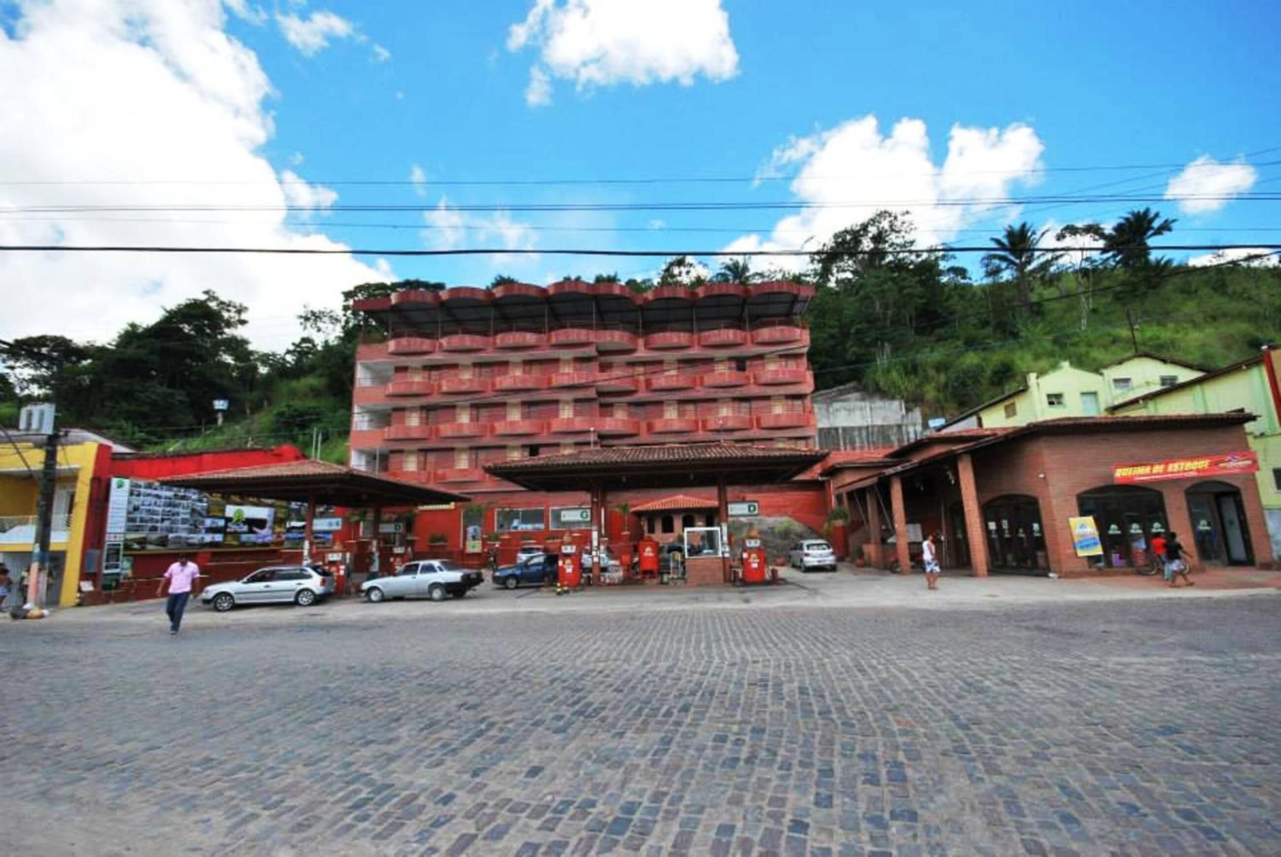 Um edifício com vários andares, fachada vermelha, área coberta com telhado e piso pavimentado.