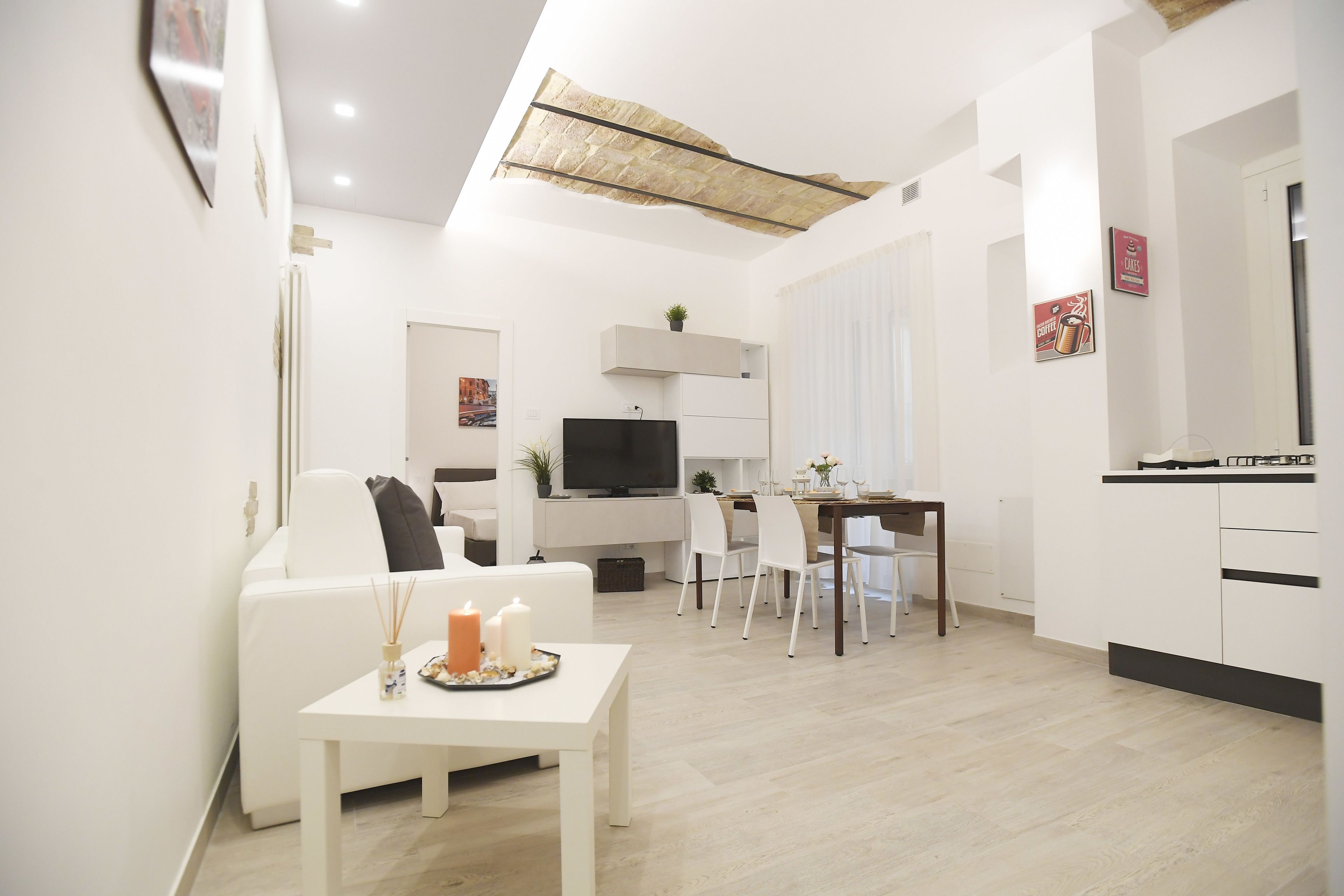 Un salon moderne avec un canapé blanc, une table à manger décorée de bougies et un téléviseur.
