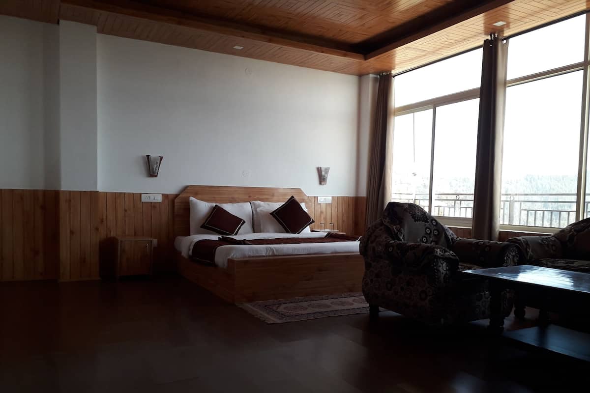 A bedroom with a wooden bed, a patterned armchair, and a view of the outdoors through large windows.
