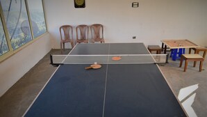 A ping pong table with a net, chairs, and a foosball table in a room with a large window. - Beyond Stay Tikker Narkanda Cottage (Theog)