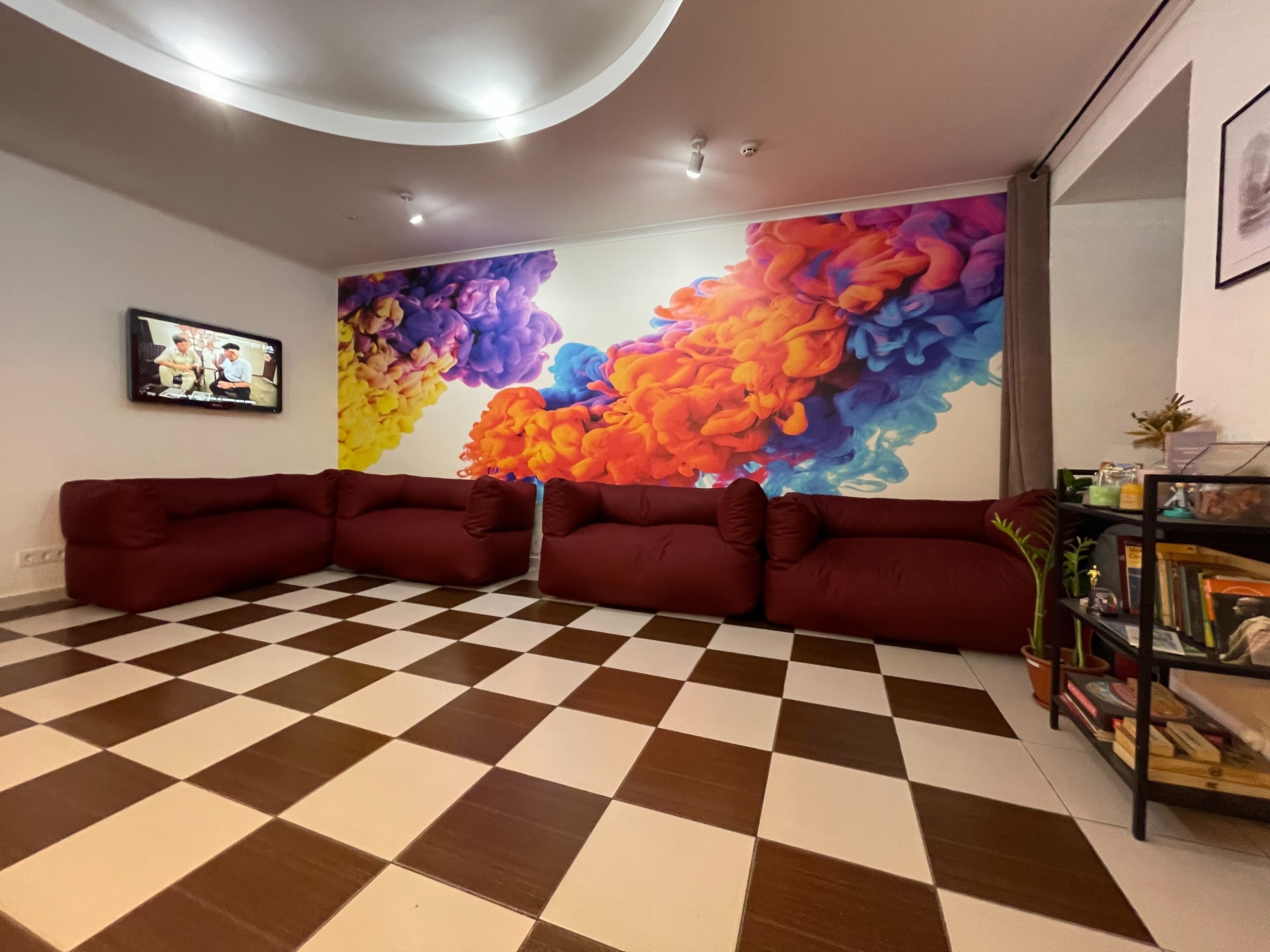 A living room with a checkered floor, a large colorful abstract mural, and a red sofa.