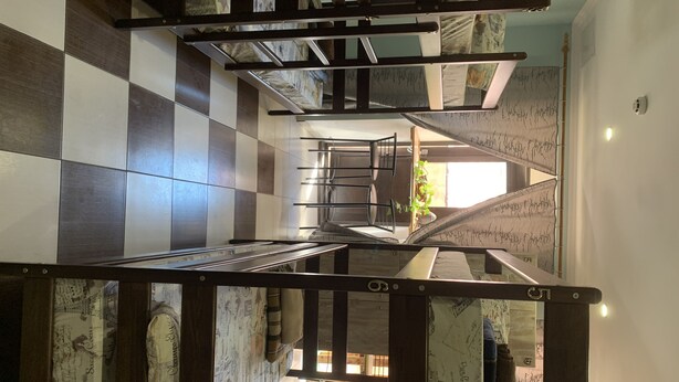 Un escalier dont le sol est recouvert d’un motif à carreaux, avec des rampes en métal et un papier peint à motifs.