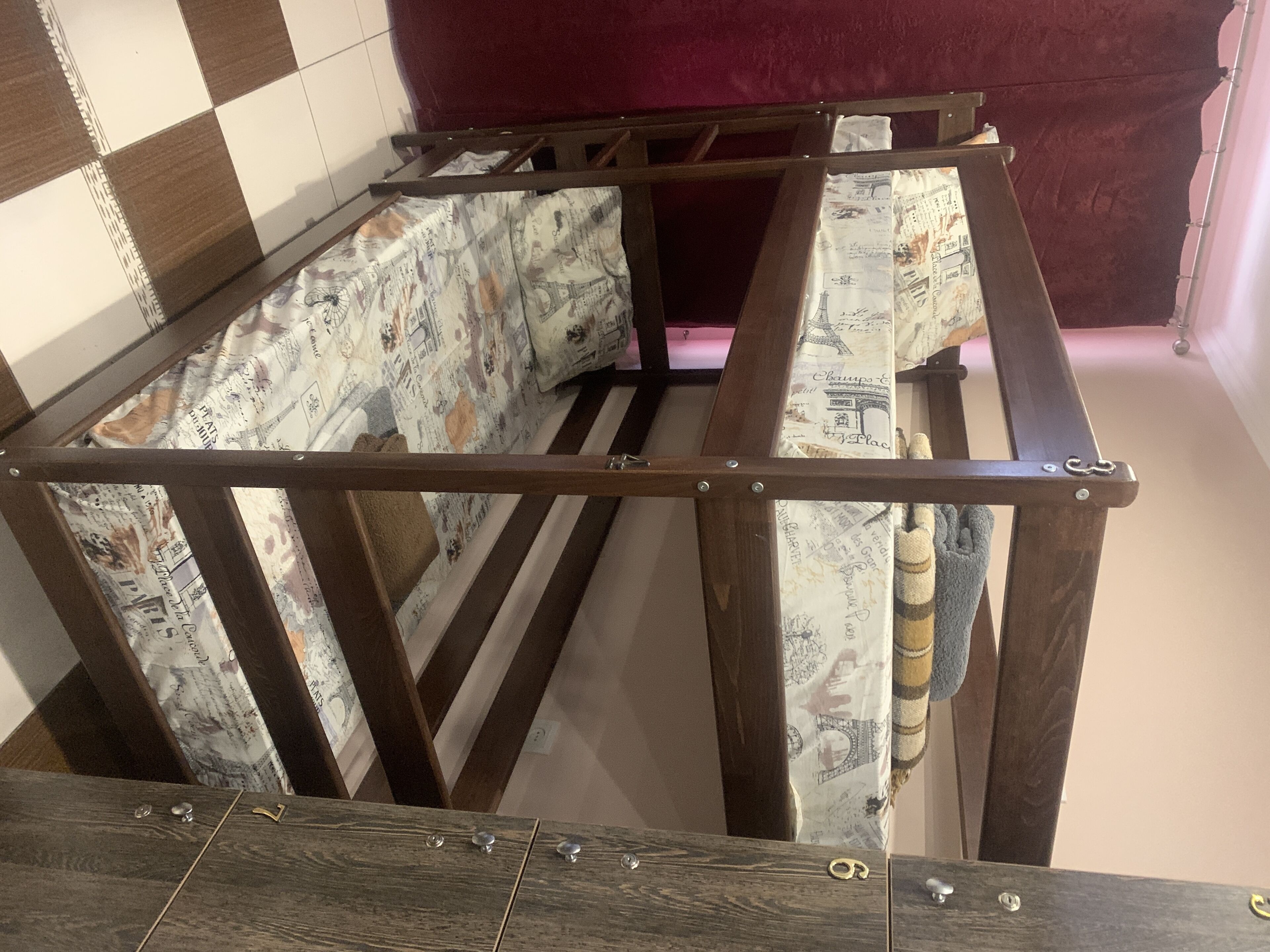 Ein Zimmer mit einem teilweise errichteten Holzrahmenbau, einem gemusterten Vorhang und einer Schachbrett-Bodenfliese.