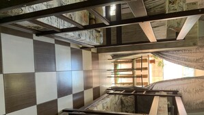 Une pièce avec un sol à carreaux, un lit recouvert d’une couvre-lit à motifs de cartes géographiques et une fenêtre donnant sur un paysage verdoyant.