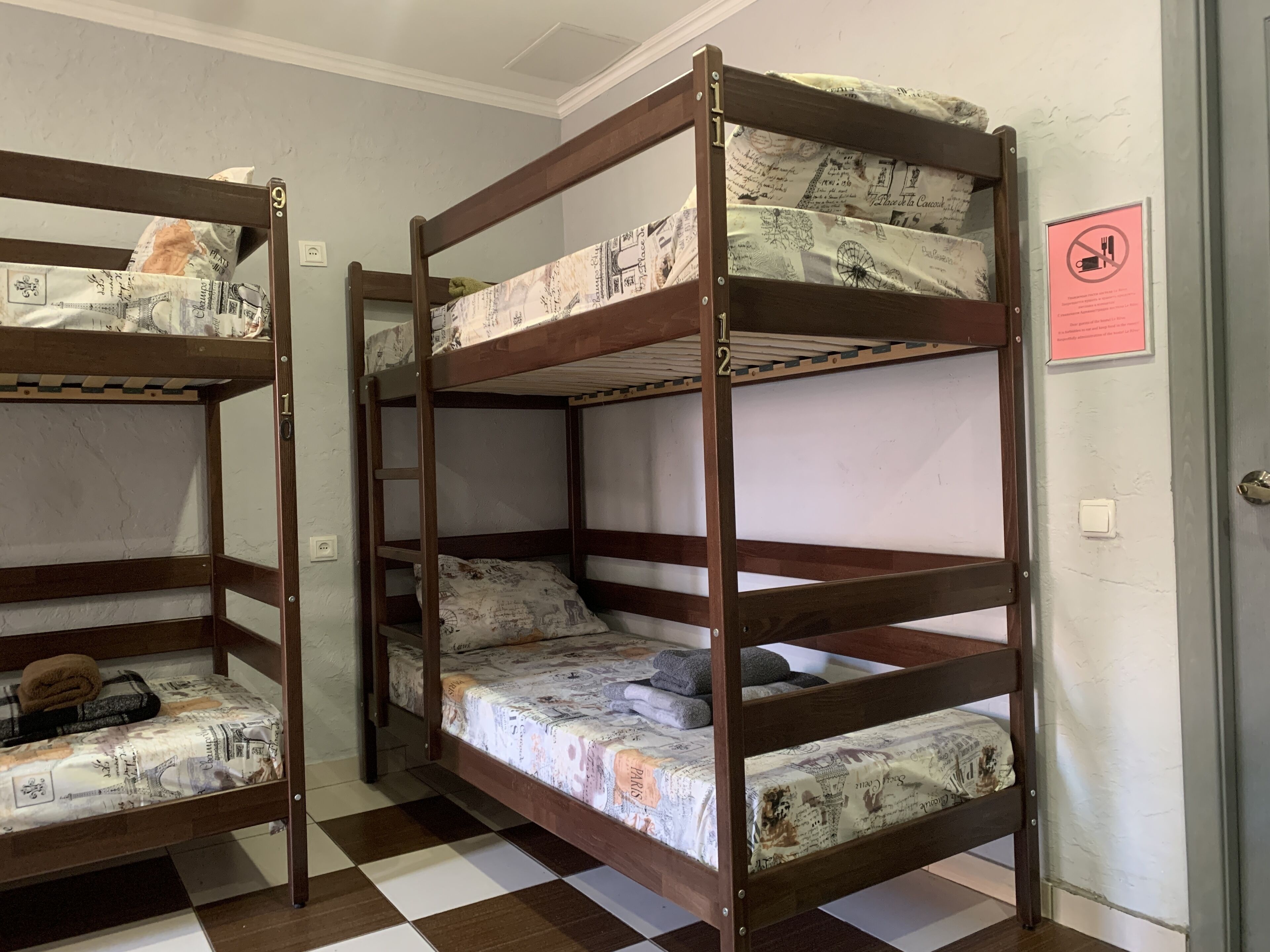 Bunk beds with newspaper bedding, a checkered floor, and a no-smoking sign on the wall.