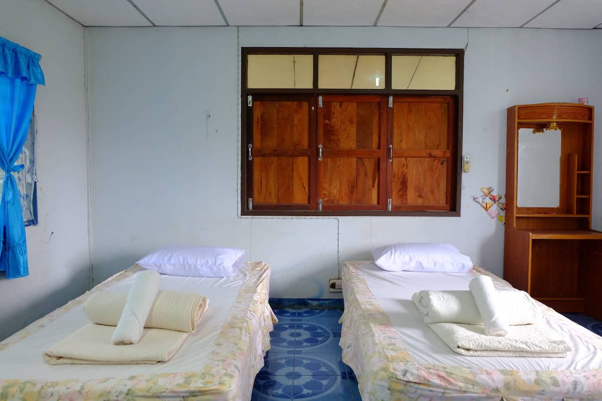 A room with two beds, each with a rolled towel and a pillow. There is a wooden wardrobe and a mirror on the wall.