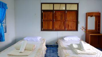 A room with two beds, each with a rolled towel and a pillow. There is a wooden wardrobe and a mirror on the wall.
