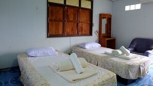 Une chambre d’hôtel avec deux lits, chacun recouvert d’une couvre-lit à motifs floraux et agrémenté d’oreillers blancs, une armoire en bois, une chaise violette et une petite table avec un miroir.