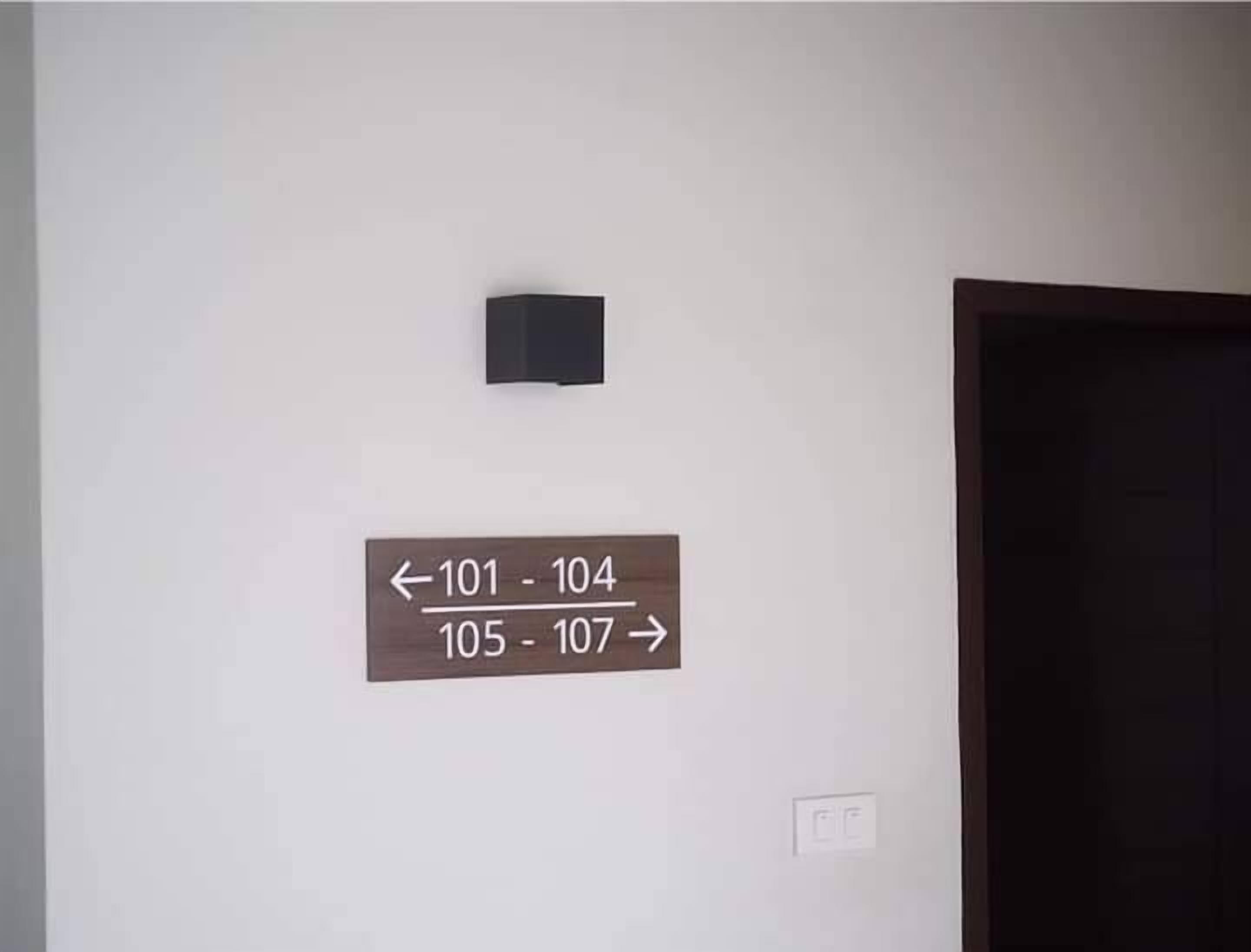 Un mur sur lequel sont affichés des panneaux indiquant la direction à suivre pour accéder aux chambres numérotées de 101 à 104 (à gauche) et de 105 à 107 (à droite).