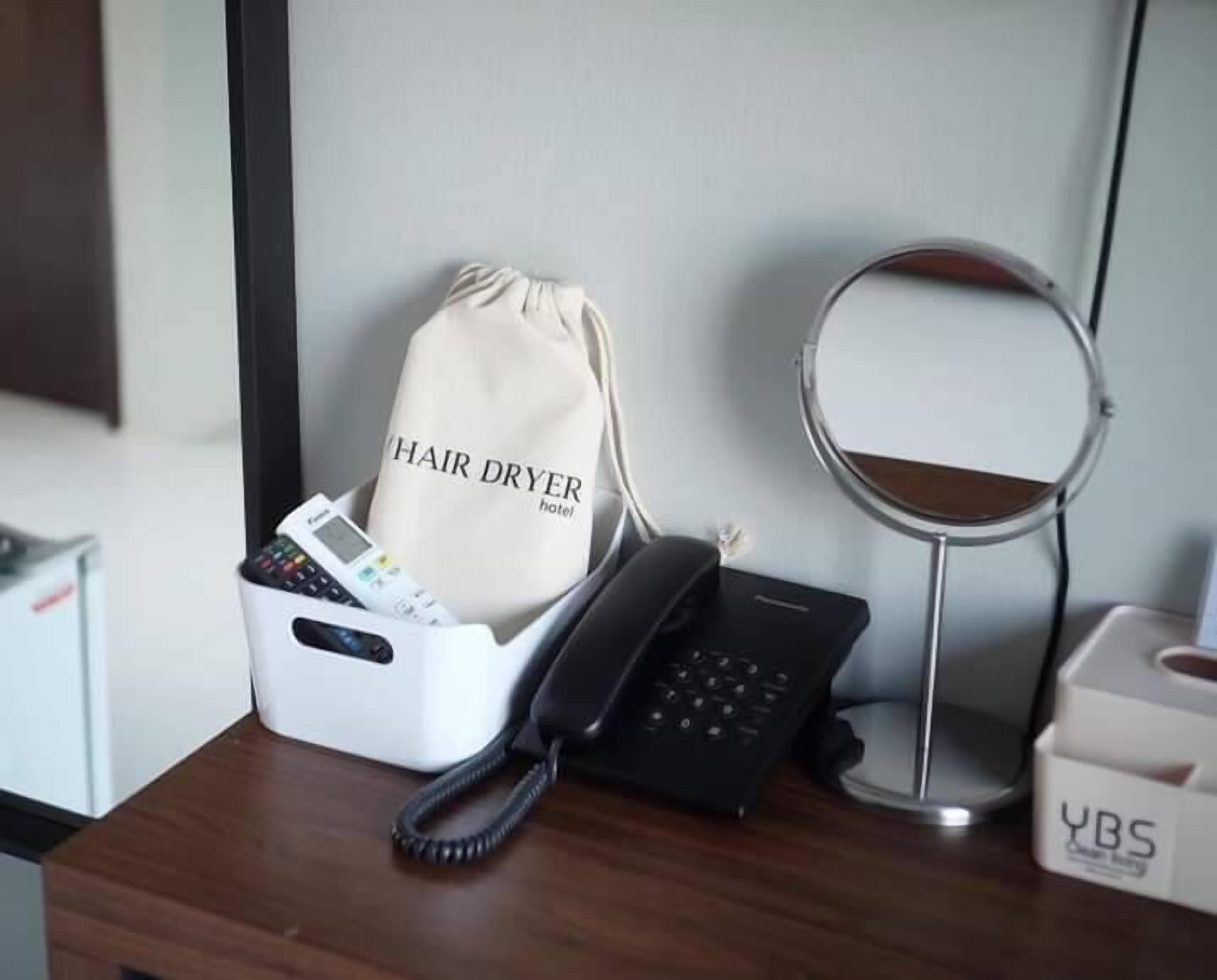 A desk with a hair dryer bag, a phone, and a compact mirror.