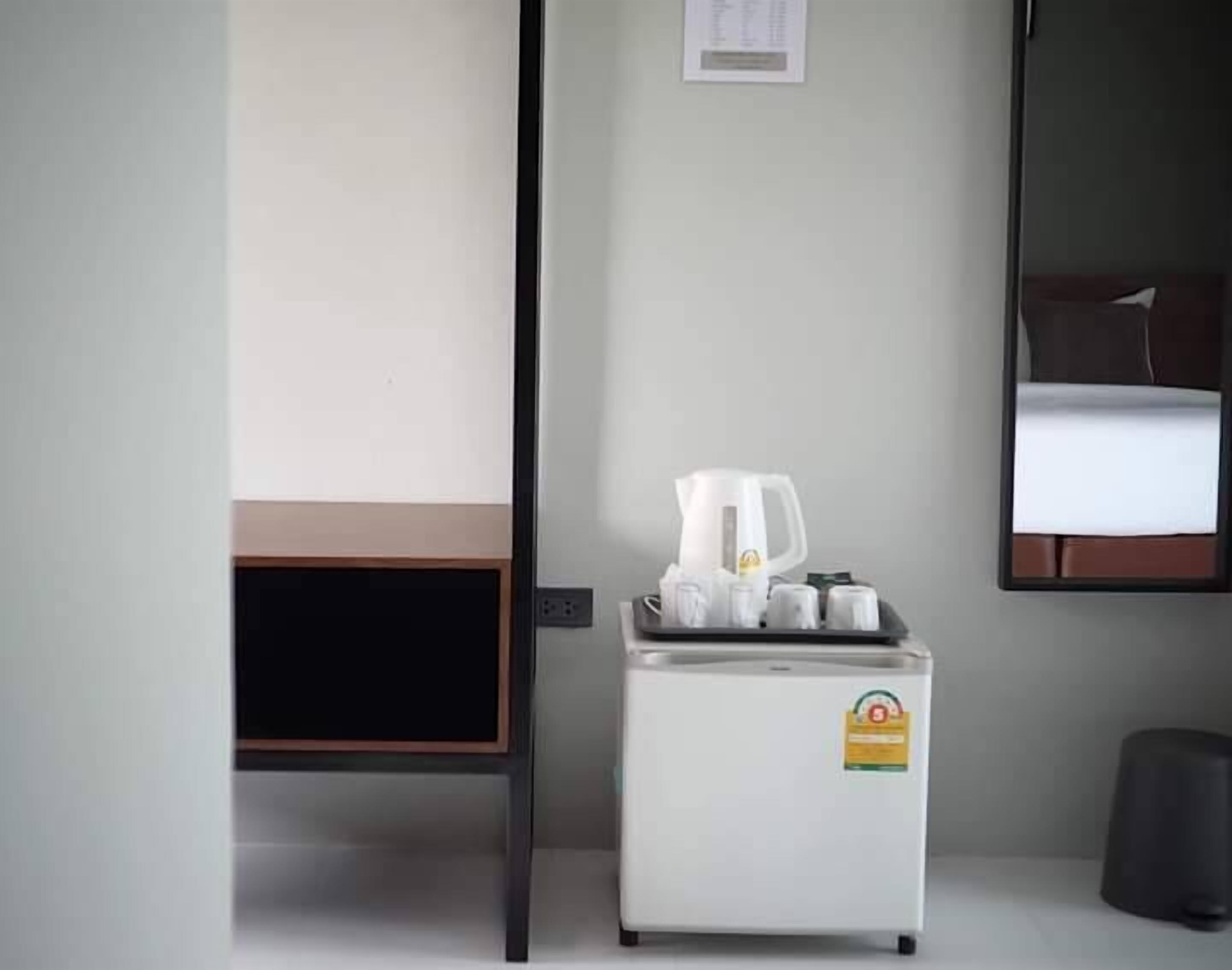 A hotel room with a bed, a small table with a kettle, cups, and a tray, and a trash bin.