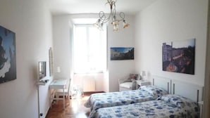 A bedroom with two beds, a desk, a chair, and a radiator.