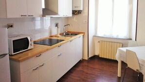 A compact kitchen with white cabinets, a microwave, a sink, and a window with blinds.