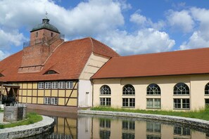 A historic building with a red-tiled roof, a brick tower, and a canal in front. - Ostsee Radlerpension Peitz (Peitz)