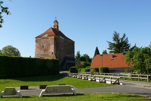 A historic stone tower with a red roof, surrounded by a well-maintained hedge and a paved pathway leading to a wooden bridge. - Ostsee Radlerpension Peitz (Peitz)