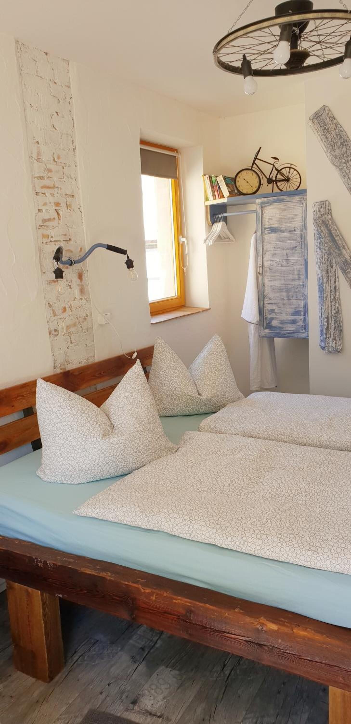 A bed with a wooden headboard, a hanging light fixture, and a window with a view of a bicycle and books.
