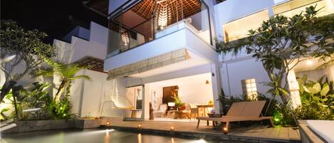 A modern two-story house with a swimming pool, outdoor seating, and lush greenery.