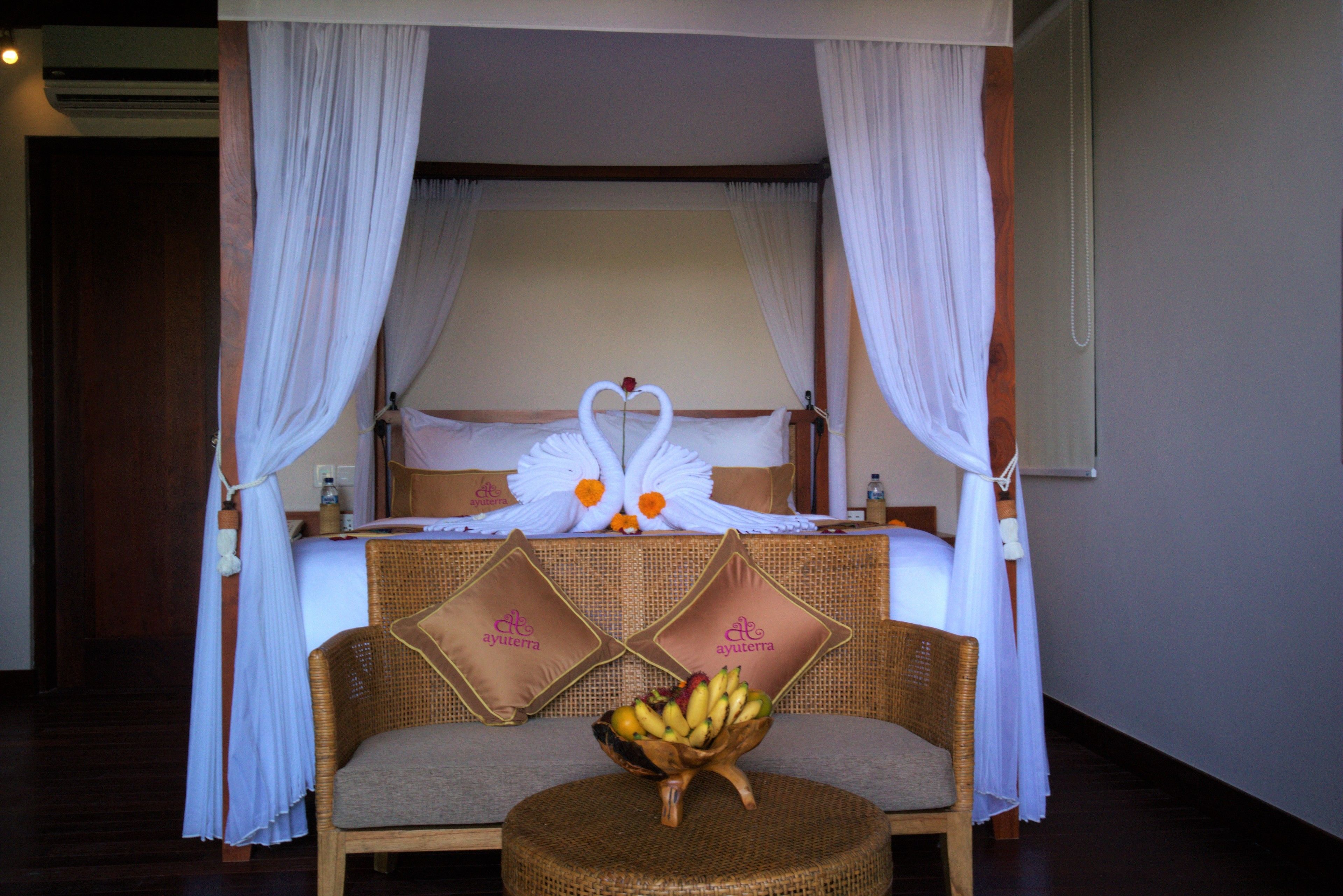 A room with a bed, a wicker sofa, a round table with a fruit bowl, and a canopy bed with white curtains.