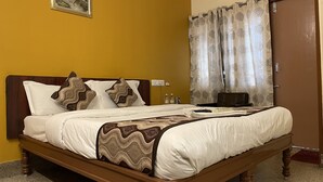Una cama bien hecha con un edredón estampado y almohadas decorativas, un aire acondicionado de pared y una puerta con cortina floral.