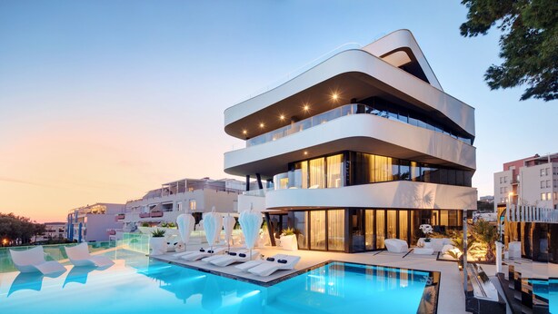 A modern multi-story building with a pool area featuring lounge chairs and umbrellas. - Posh Residence Luxury Suites (Split)