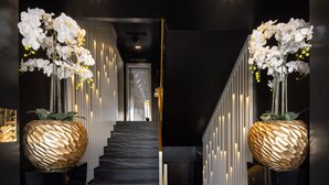 A modern reception area with a marble staircase, white orchids in large vases, and a sleek, dark interior design. - Posh Residence Luxury Suites (Split)