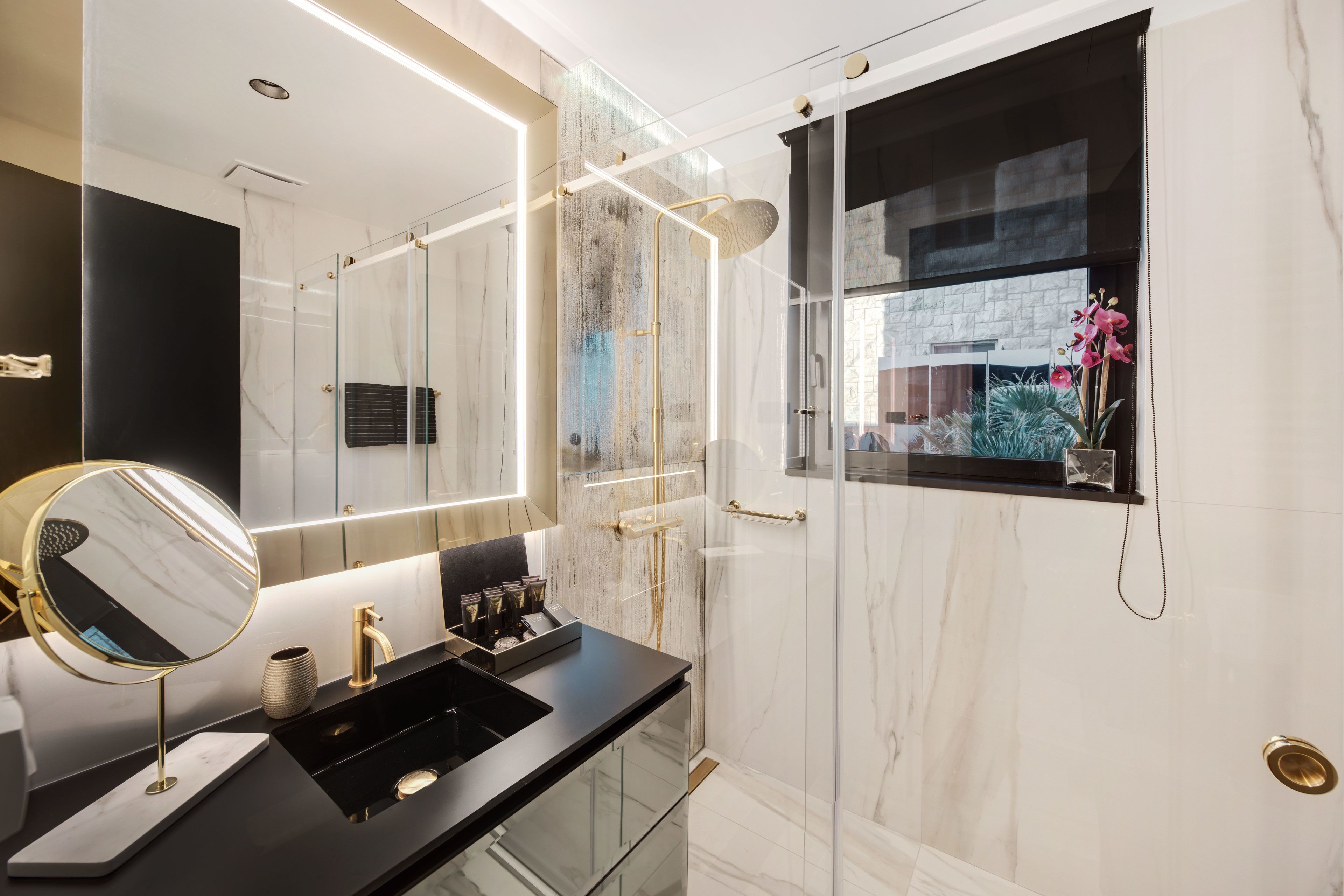 Un baño moderno con cabina de ducha de vidrio, un espejo grande y encimera negra.
