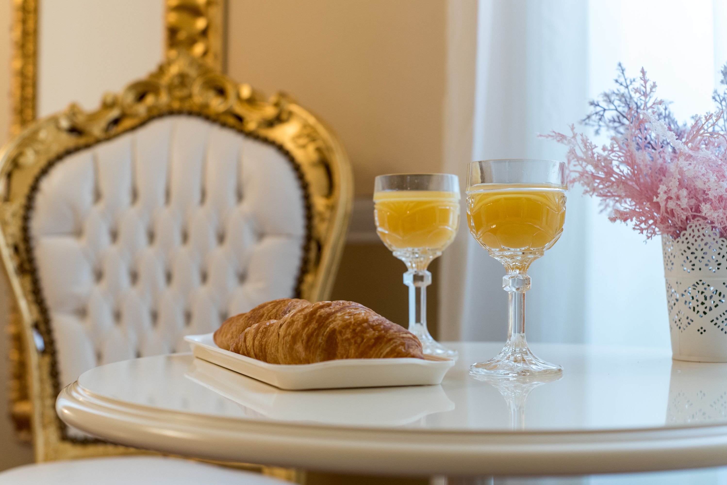 A table with a croissant, two glasses of orange juice, and a vase with pink flowers.