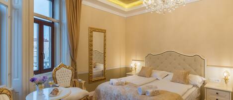A luxurious bedroom with a large bed, a chandelier, and a dining area with a table and chairs.