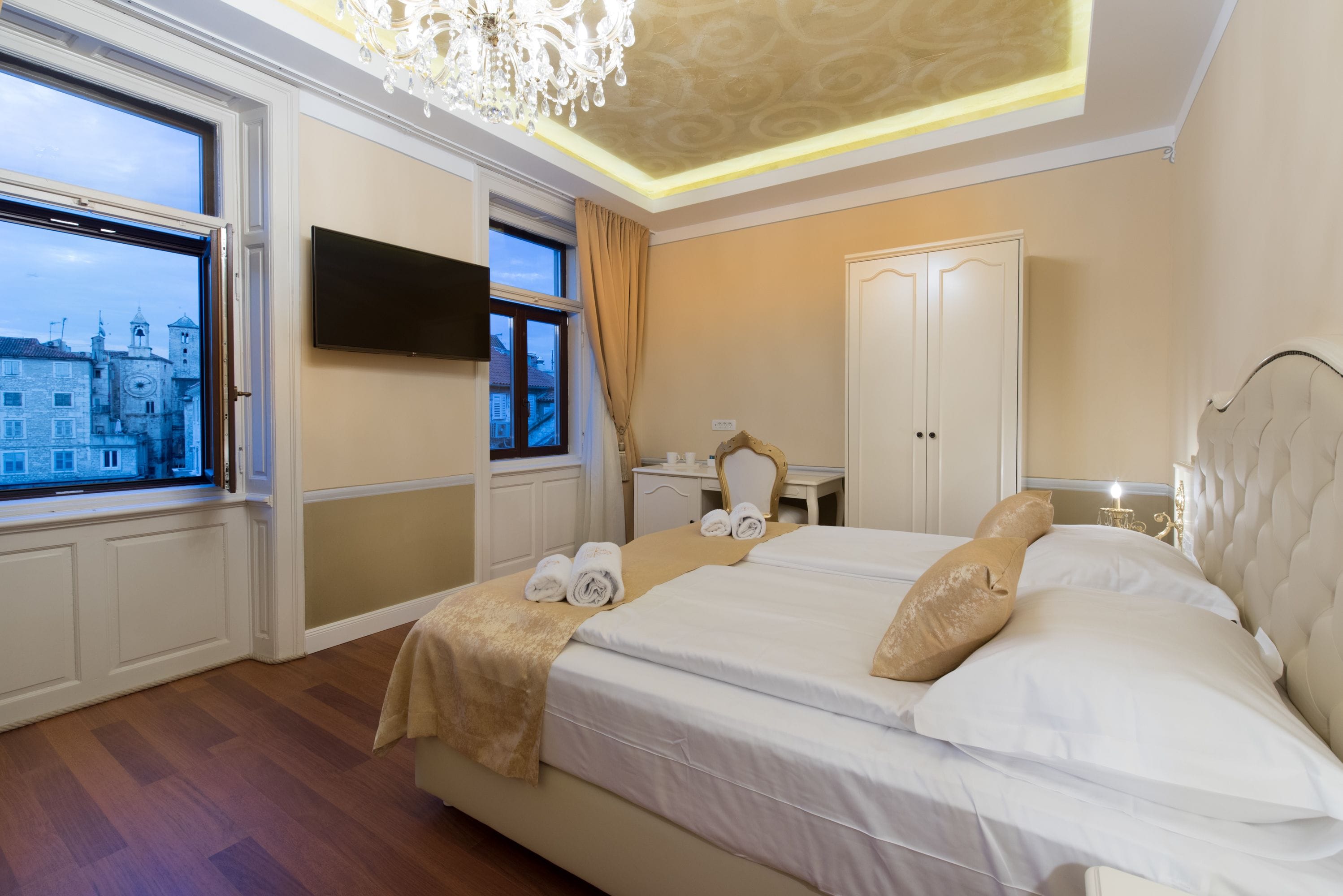 A hotel room with a large bed, a television, a desk, and a view of a historic building through the window.