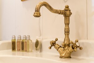Un baño con un grifo de latón y tres botellas de jabón líquido en el lavabo.