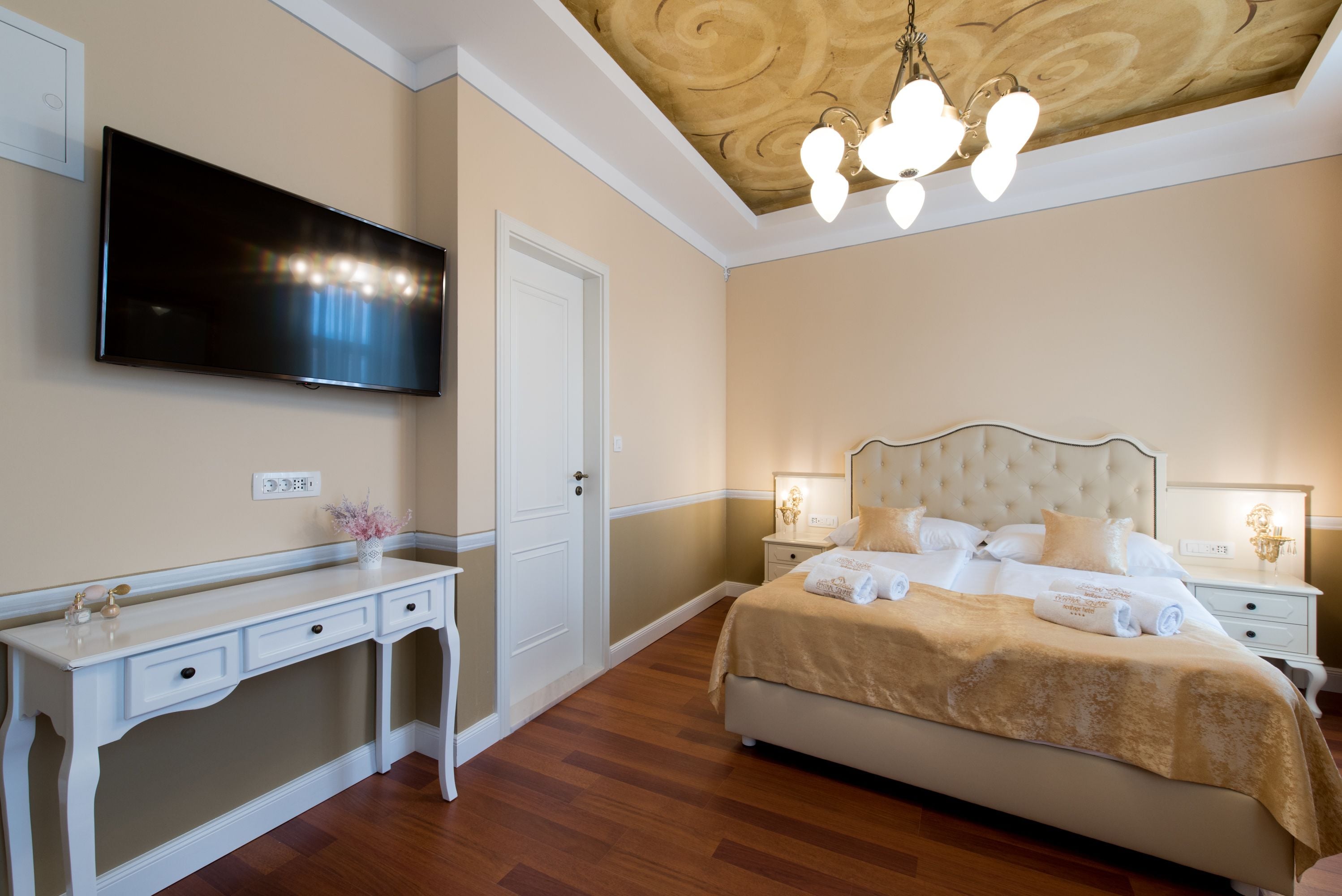 A bedroom with a bed, bedside tables, a TV mounted on the wall, and a desk with drawers.