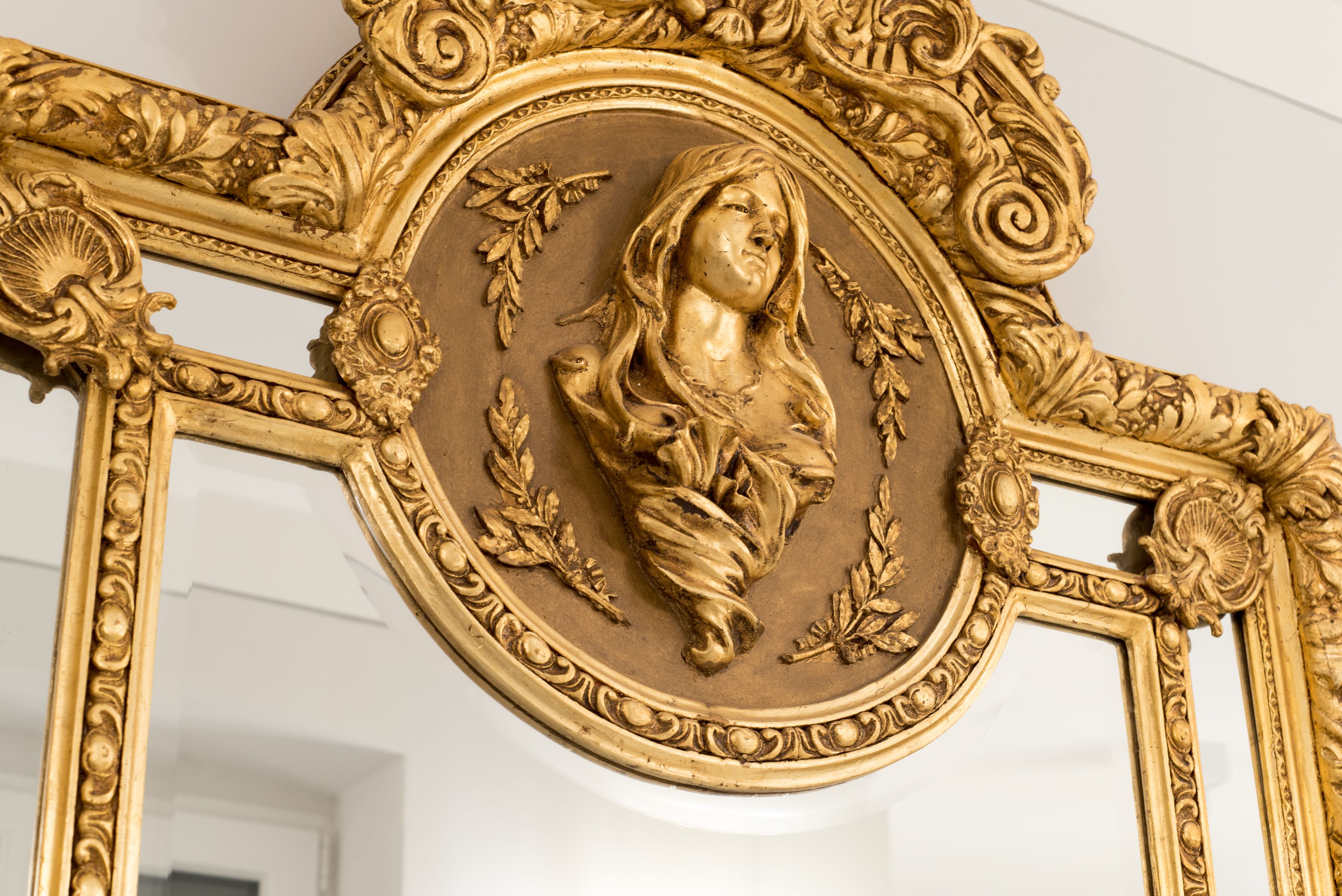 A detailed golden ornate mirror frame with intricate designs and a central relief sculpture.