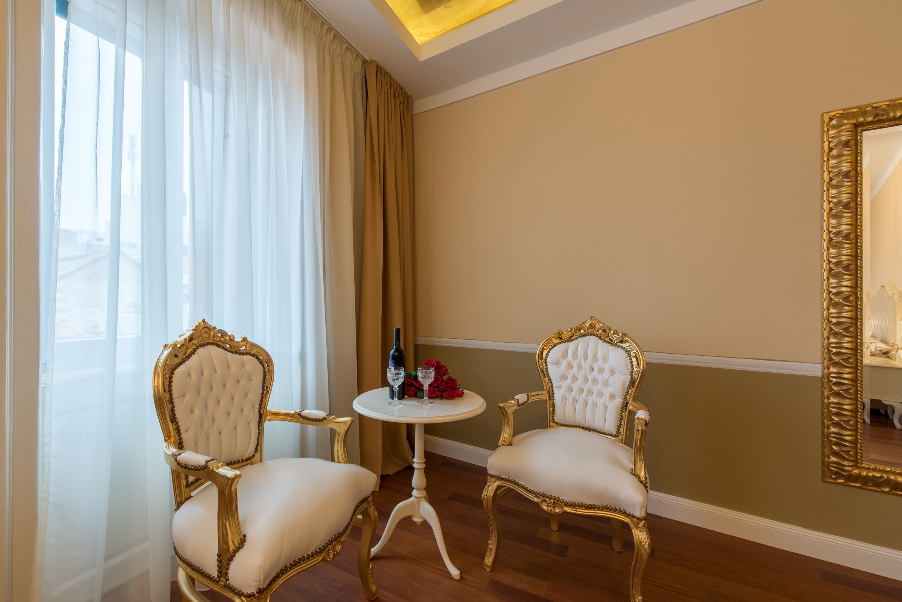 Une pièce comprenant deux fauteuils richement décorés, une petite table ronde avec une bouteille et des verres, et un grand miroir accroché au mur.