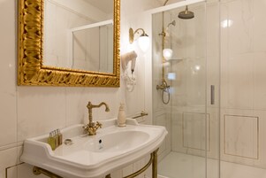 A bathroom with a white sink, gold fixtures, a large mirror with a gold frame, and a glass-enclosed shower.