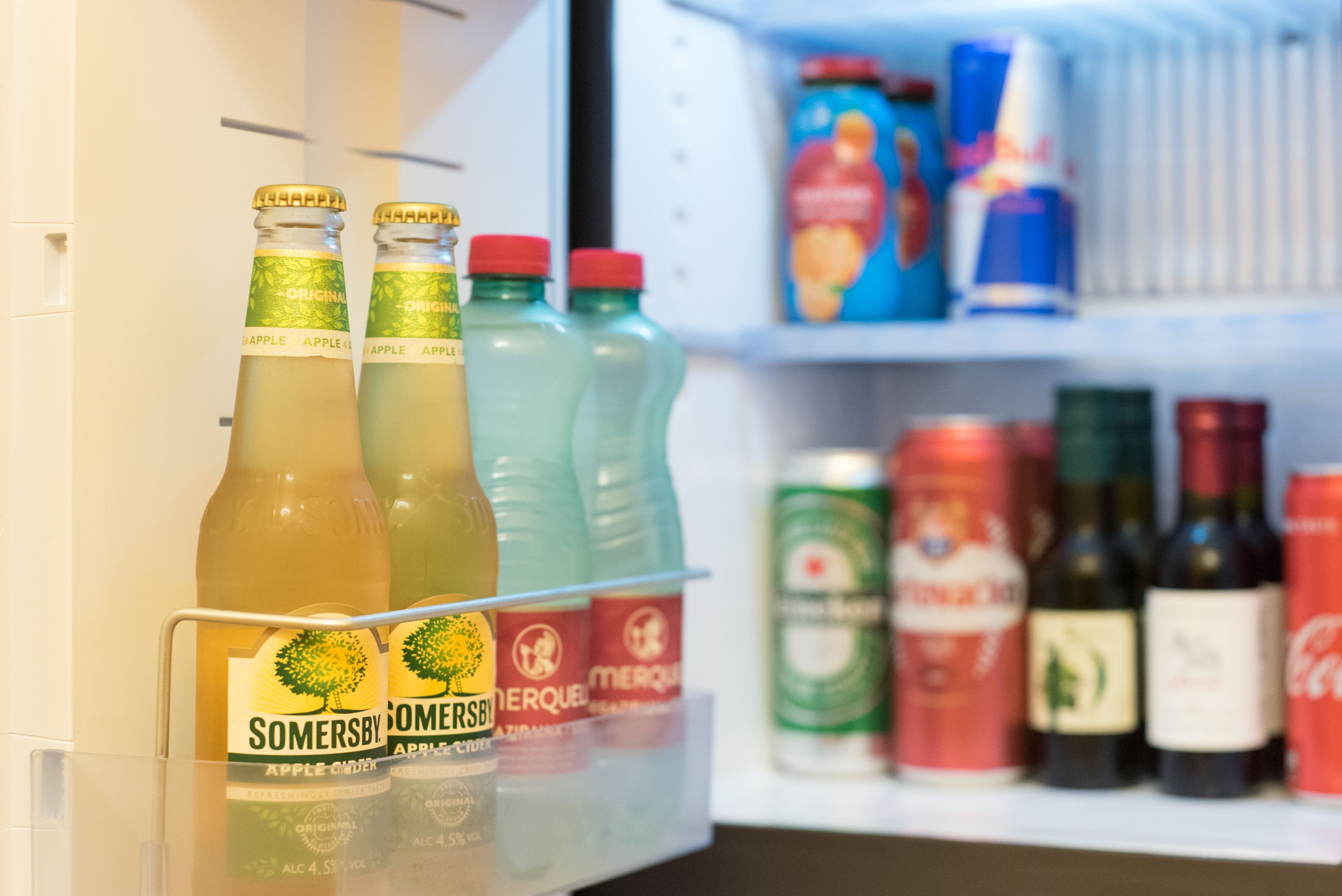 Un refrigerador lleno de bebidas, incluyendo botellas de sidra de manzana Somersby y diferentes gaseosas.