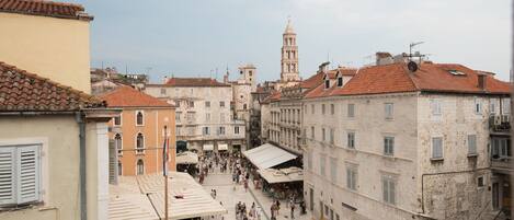 A bustling square with historic buildings, a prominent clock tower, and outdoor seating areas.