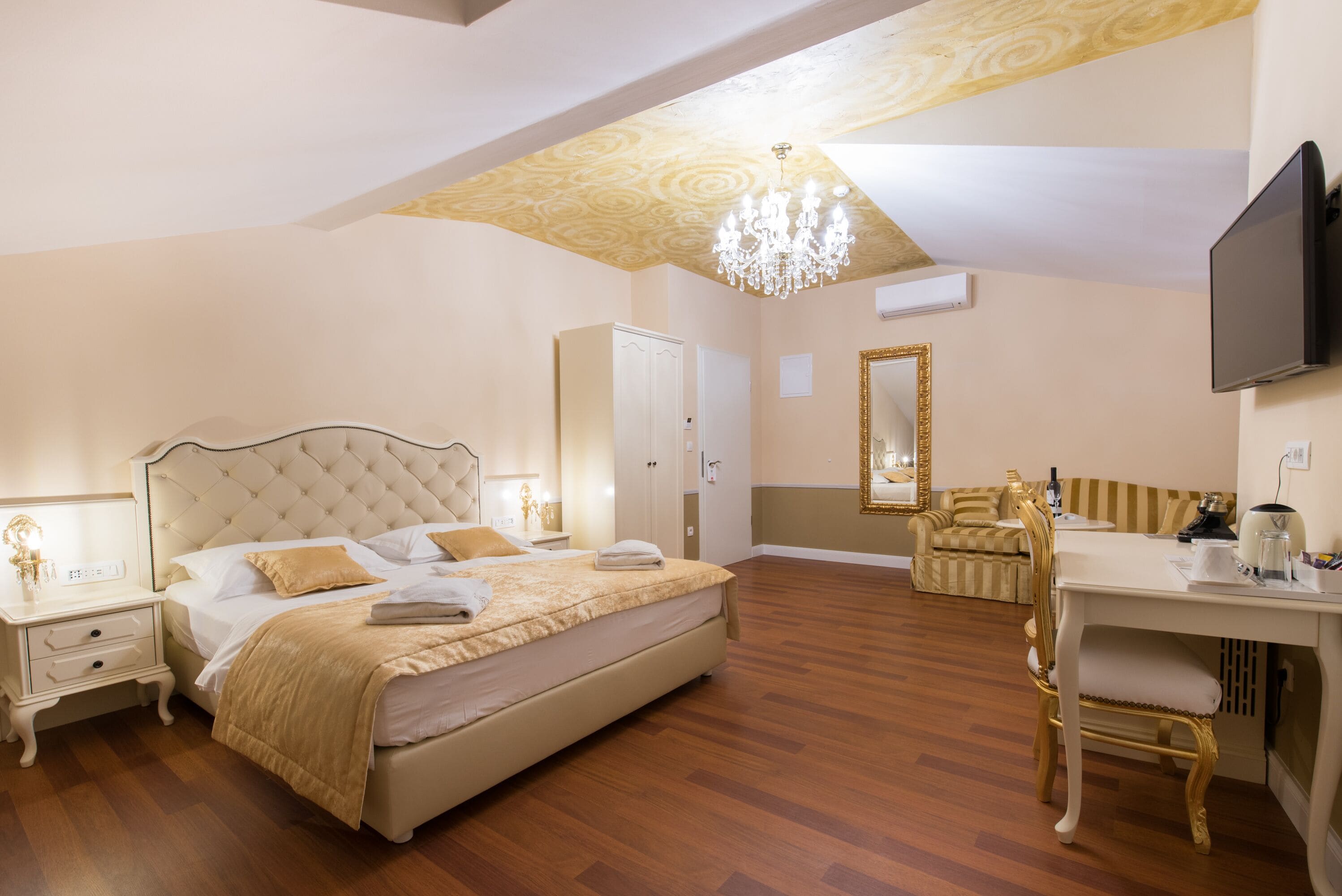 Une chambre à coucher avec un grand lit, un bureau, une chaise, une télévision et un lustre.