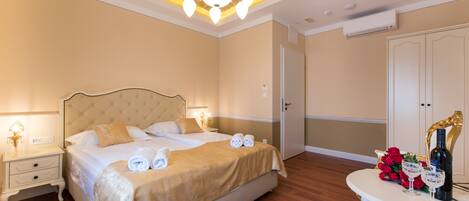 A hotel room with a large bed, bedside tables, a chandelier, and a table with a bottle and glasses.