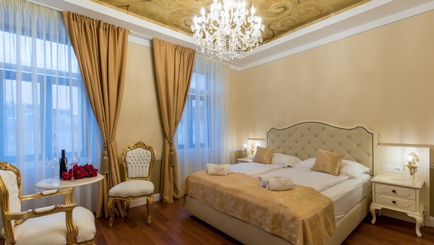 A luxurious bedroom with a large bed, a chandelier, and a view of the city through large windows. - Central Square Heritage Hotel (Split)