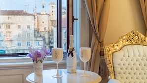 A table with a bottle of Moët champagne and two glasses, a vase with flowers, and a view of historic buildings through a window. - Central Square Heritage Hotel (Split)
