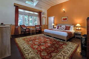 A hotel room with a large bed, two bedside tables with lamps, a desk with a chair, a large window with curtains, and a red and beige patterned rug. - Brij Villa, Dalhousie - A Colonial Luxury Retreat (Dalhousie)