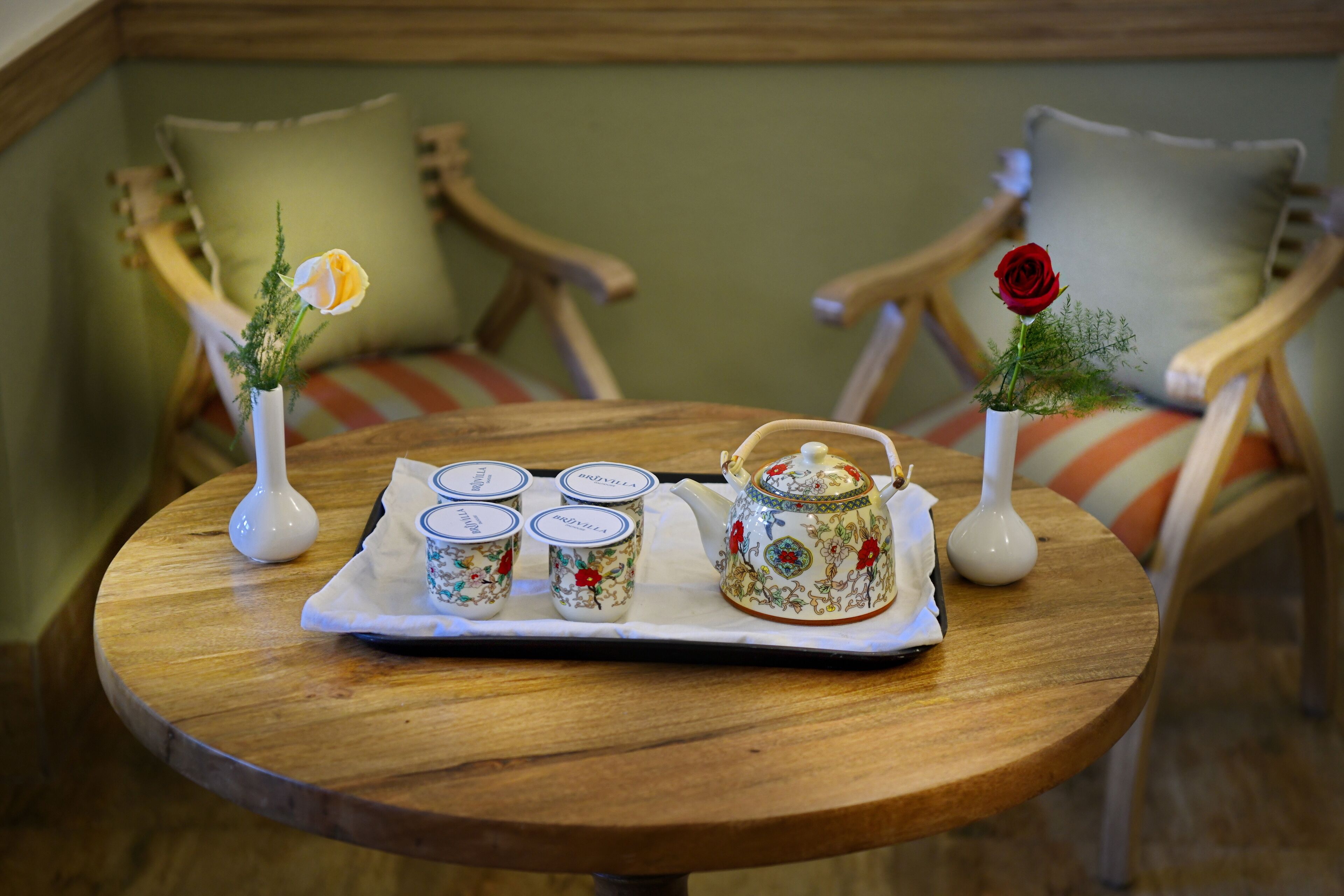 A wooden table with a tray holding four white ceramic cups and a decorative teapot.