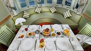 A dining table set for a meal with various dishes, surrounded by a green cushioned bench with striped pillows. - Brij Villa, Dalhousie - A Colonial Luxury Retreat (Dalhousie)