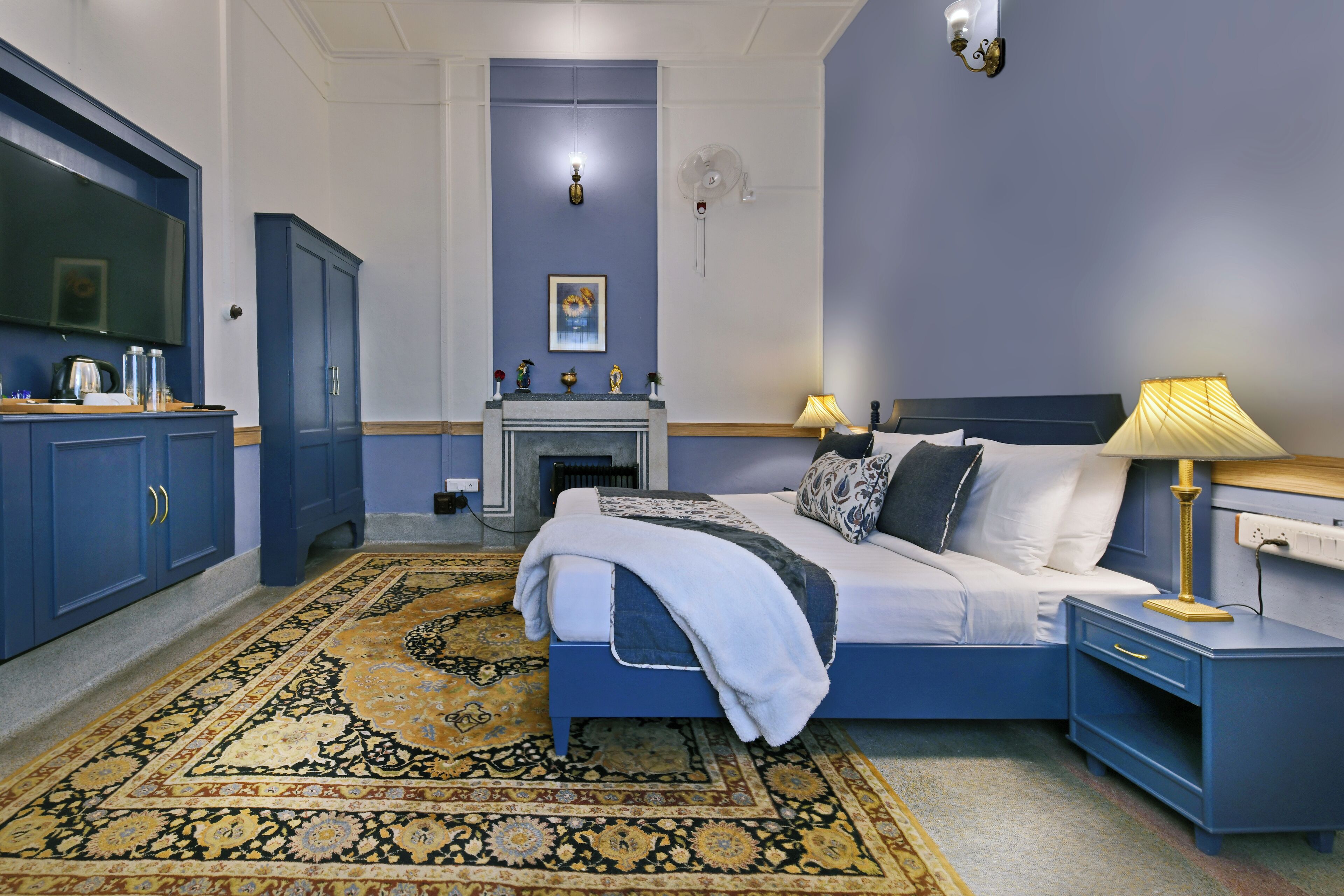 A bedroom with a bed, nightstands, a dresser, a television, and a fireplace.