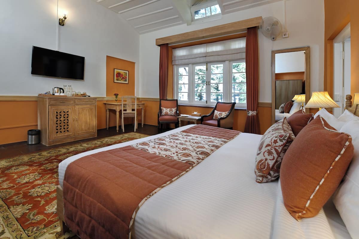 Habitación de hotel con una cama grande, un escritorio, una silla, un televisor y una ventana con cortinas.