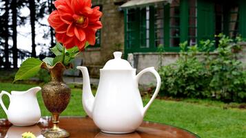 Uma mesa com um jarro branco, uma chaleira branca e um vaso com uma flor vermelha.