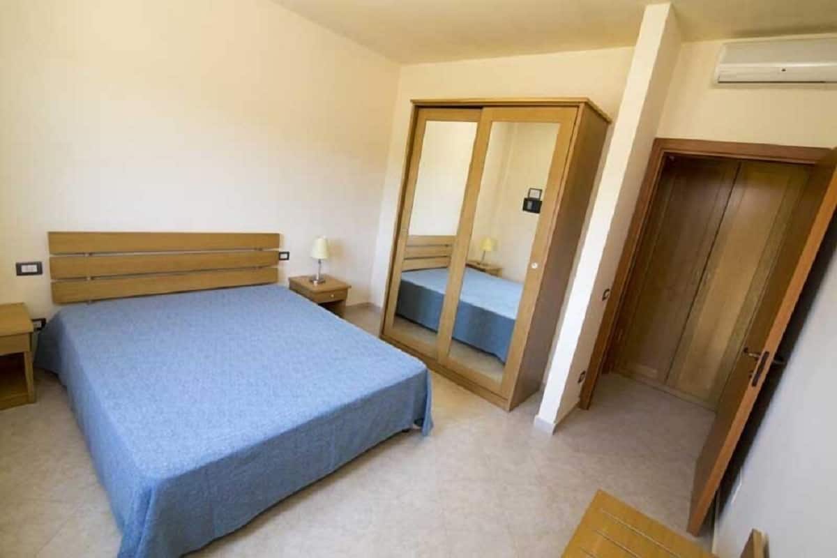 A bedroom with a bed, a nightstand, a wardrobe, and a mirror.